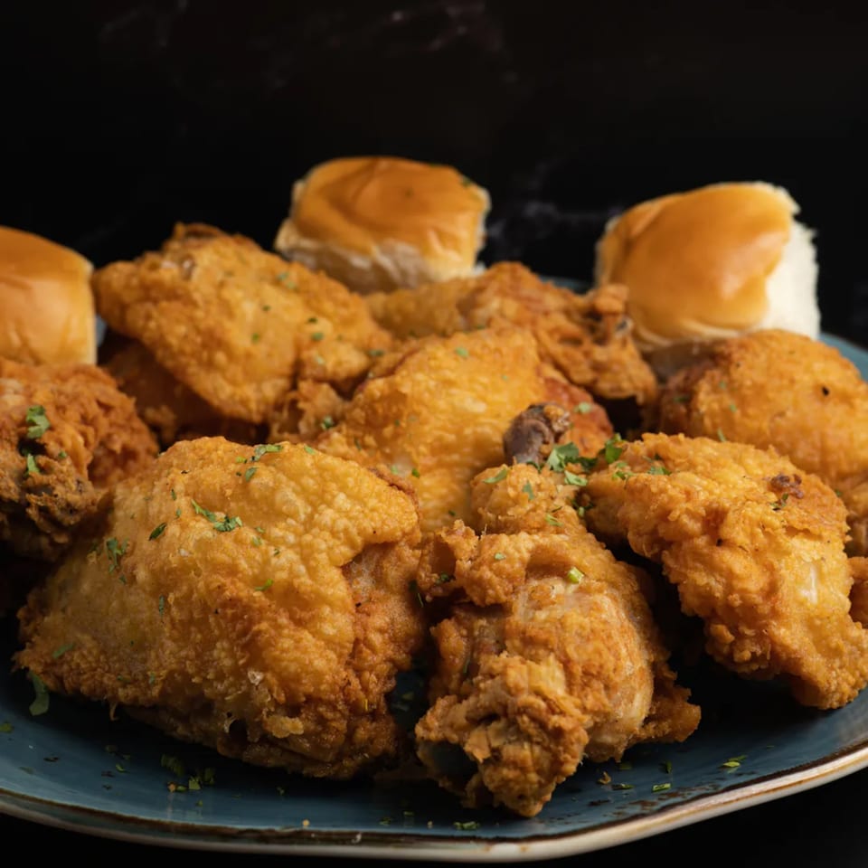 A blue plate piled high with golden-brown fried chicken pieces and dinner rolls.